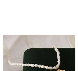 Detail of natural baroque pearl necklace with a hammered gold coin pendant on green velvet