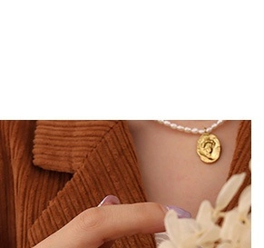 Detail of a pearl necklace with a vintage gold coin pendant worn on a female neck