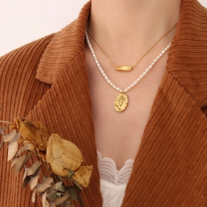 Layered gold snake chain and pearl necklace with embossed vintage pendant on a model