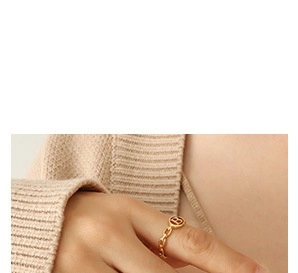 Detail of gold chain texture ring with letter B coin on a finger with knitwear background