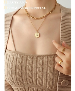 Close-up of gold-plated portrait coin necklace and chunky Cuban chain on knitwear