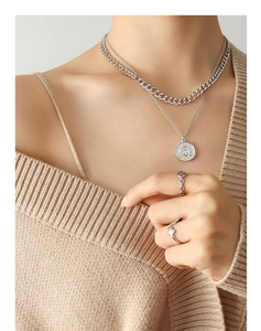 Close-up of double-layer silver necklace and rings set on soft knitted fabric