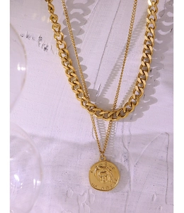 Close-up of gold double-layered necklace with Medusa coin pendant on white wooden texture