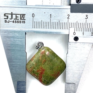 Medición del colgante cuadrado de unakita de 24x28mm con un calibre sobre fondo blanco