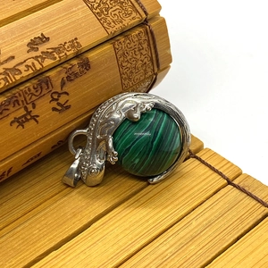 Macro detail of lizard-shaped silver pendant holding a round green malachite gemstone