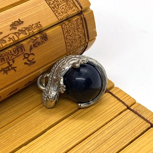 Detailed view of a silver lizard pendant clutching a deep blue round gemstone ball