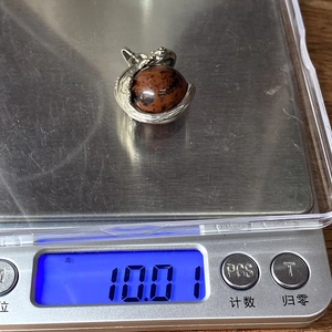 Detail of a round red and black gemstone pendant weighing 10.01 grams on a scale