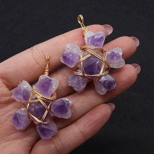 Macro detail of wire-wrapped purple amethyst flower pendants held by hand for scale