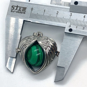 Macro shot measuring a heart-shaped angel wing pendant with a green malachite stone