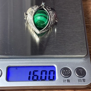 Detailed view of heart-wing pendant with green stone on digital scale weighing 16.00g