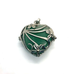 Locket detail showing silver flower pattern and heart-shaped green stone insert