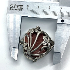 Macro shot measuring a heart-shaped goldstone pendant with a floral hollow metal cage