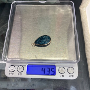 Detailopname van een druppelvormige blauwe steen hanger met gouden rand gewogen op een weegschaal