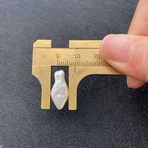 Measuring irregular baroque freshwater pearl length using brass calipers on dark surface
