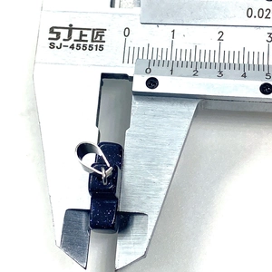 Detailed measurement of blue goldstone cross pendant width using a metal caliper