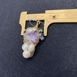 Macro detail of handmade amethyst and pearl grape pendant with wire wrapping on brass caliper