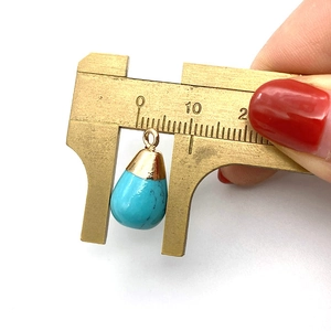 Macro shot of turquoise teardrop pendant being measured with a brass caliper showing 10mm width