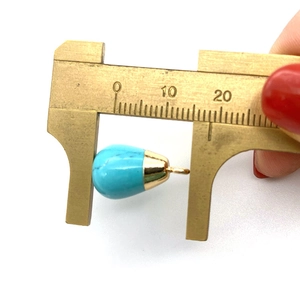Macro shot of measuring a turquoise teardrop pendant size with a brass caliper tool