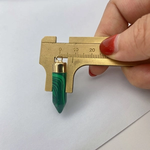 Measuring the 8mm width of a green malachite hexagonal prism pendant with a brass caliper
