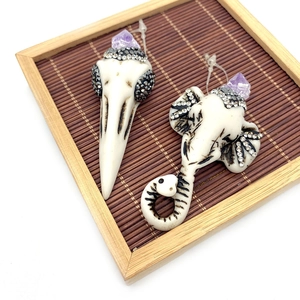 Gothic skull earrings with purple crystals and bird skull design on bamboo mat