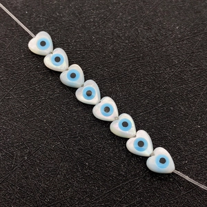 Macro detail of heart-shaped shell beads with blue evil eye pattern for DIY jewelry