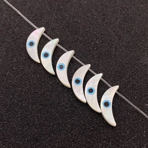 Makroaufnahme von halbmondförmigen Muschelperlen mit Evil Eye Muster auf Schwarz