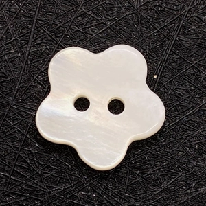 Macro detail of white flower shell button with dual holes on a dark textured background
