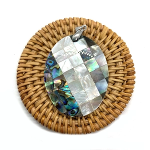 Macro shot of oval shell pendant with abalone and mother of pearl mosaic on a woven mat