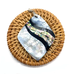 Macro shot of a diamond-shaped natural shell pendant with abalone inlay on a woven mat