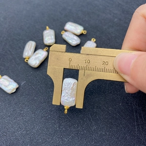 Caliper measuring a white rectangular freshwater pearl pendant with golden bail