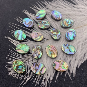 Macro shot of oval abalone shell beads with iridescent glow on white feathers