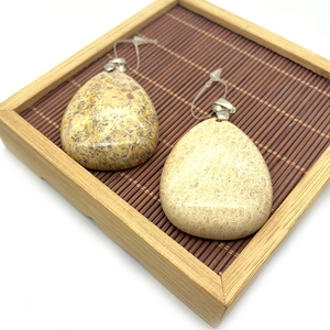 Pendentif goutte en pierre naturelle marron avec motifs floraux sur plateau bambou
