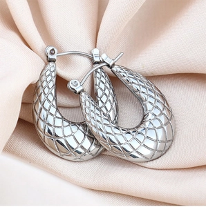Detail shot of silver U-shaped earrings with diamond-pattern texture on satin fabric