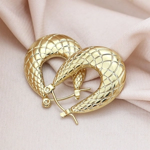 Detailed macro view of gold U-shaped earrings with textured grid patterns on silk background