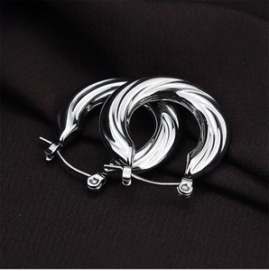 Detail of silver twisted U-shaped hoop earrings with polished texture on dark fabric