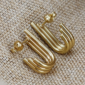 Orecchini a forma di U in oro lucido su sfondo di lino materico elegante