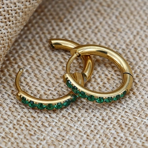Elegant gold huggie hoop earrings with green zircon stones on a beige textured fabric