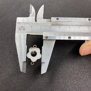 Measuring white shell flower charm with 18mm diameter using a metal caliper tool