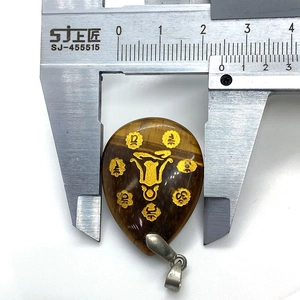 Macro shot measuring width of teardrop tiger eye stone pendant with golden symbol
