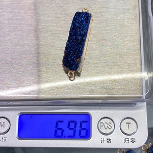 Macro-opname van een rechthoekige blauwe kristallen hanger van 6,96g op een weegschaal