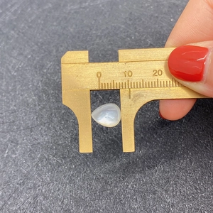 Detailed dimension measurement of natural white teardrop shell bead with brass caliper