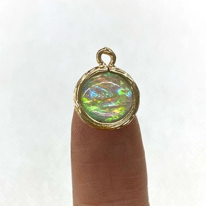 Macro view of a round opal pendant with gold plated frame held between fingers