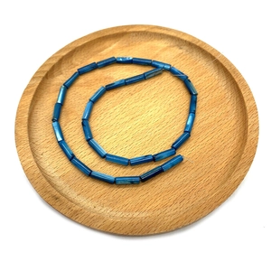 Dettaglio macro di perle in conchiglia naturale tubolare blu scuro in un vassoio di legno