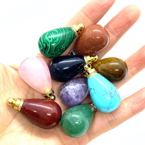 Selection of teardrop gemstone perfume bottle pendants held in hand on white background