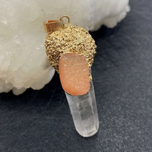 Macro detail of natural druzy stone pendant with raw quartz and gold electroplated edge