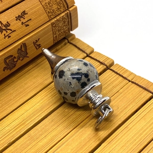 Close-up of Dalmatian Jasper sphere pendant with silver metal fittings on bamboo background