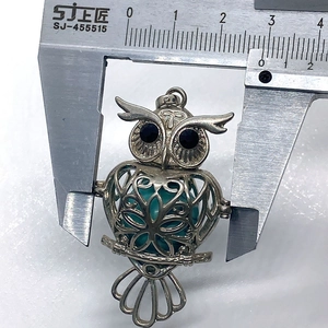 Detailed size measurement of a silver owl pendant with green stone bead and ruler