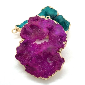 Détail des pendentifs en cristal druzy magenta et cyan avec bordure dorée polie