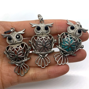 Three retro owl pendants with hollow cage design holding colorful natural stones on a hand
