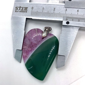 Primer plano de un colgante de corazón de ágata verde y púrpura medido con un calibre